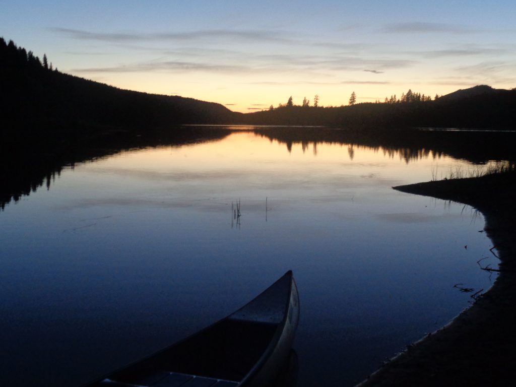 En kanot ligger vid stranden i en av sjöarna i Rottnan i norra Värmland. Vid horisonten skymmer kvällen, vattnet ligger som en spegel.