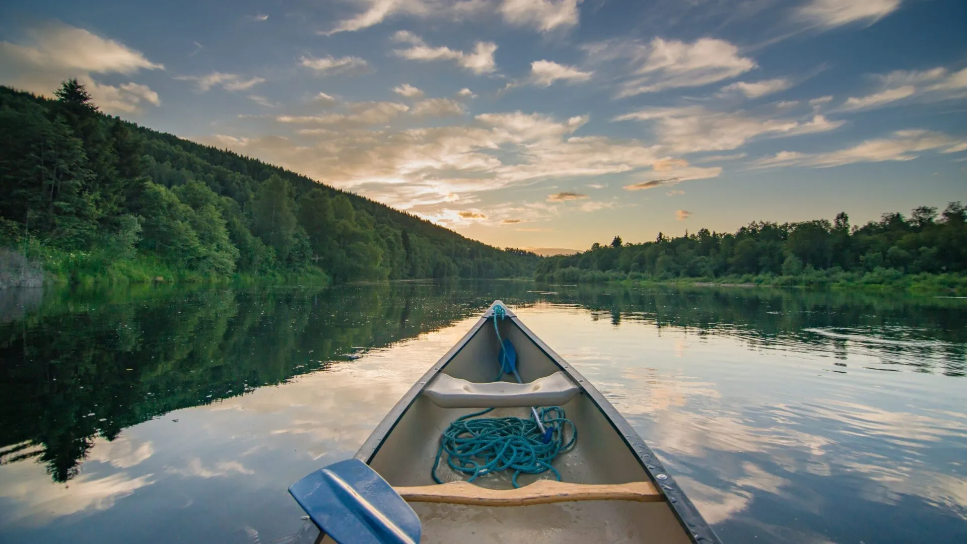 En kanot flyter på vattnet i Klarälven i norra Värmland, skogsbeklädd strand på båda sidor som möts vid horisonten, himlen visar fina skymningsfärger